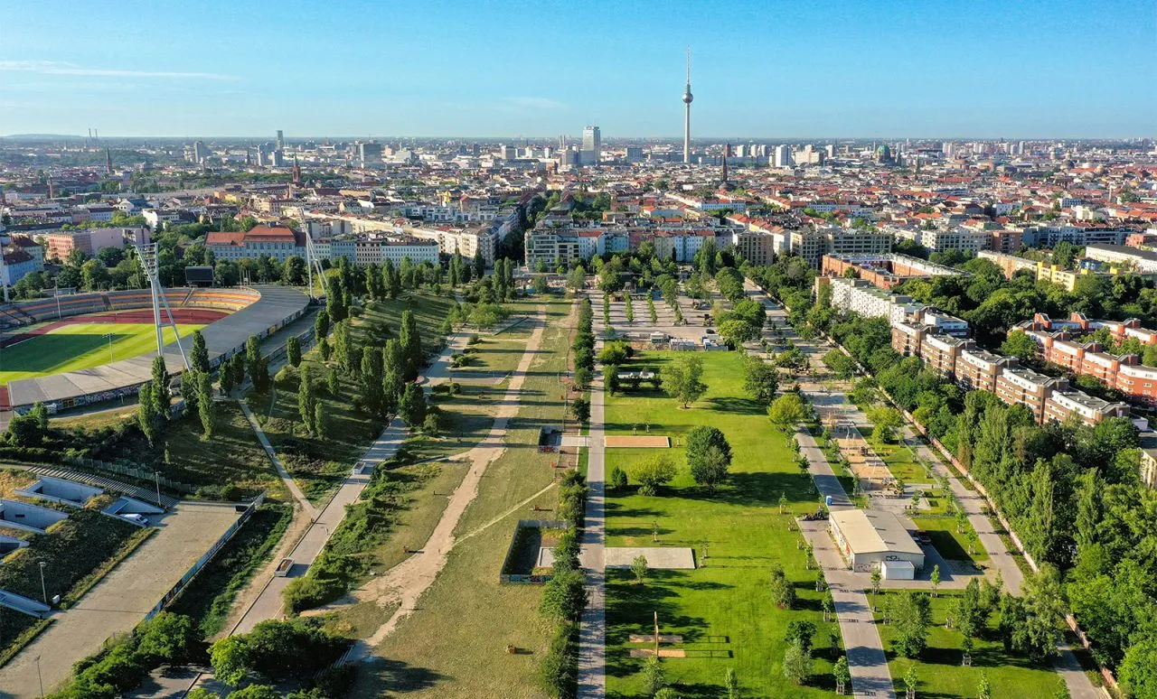 Aerial view of urban park with green spaces, pathways, and city skyline featuring a TV tower.