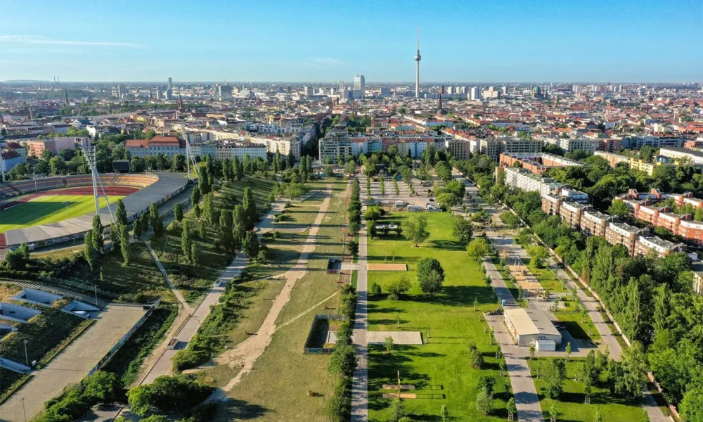 Aerial view of urban park with green spaces, pathways, and city skyline featuring a TV tower.